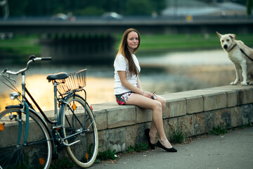 Young girl with the bike sitting on the promenade of the river.