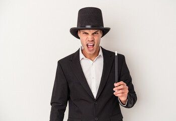 Young magician caucasian man holding a wand isolated on white background screaming very angry and aggressive.