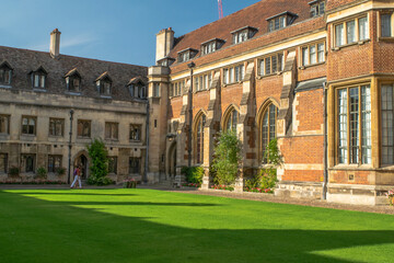 University Students walk along the lawn of historical bricked Christ's College Court with ornate...