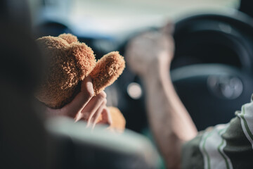 Child's hand holding a brown teddy bear sit in the front seat next to the driver, driving safety concept.