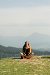 Front view of brunette female sitting in pose of lotus in mountains and doing meditation. Beautiful...