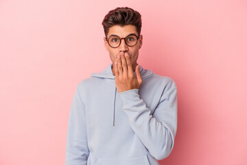 Young caucasian man isolated on pink background shocked, covering mouth with hands, anxious to discover something new.