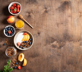 Flat lay delicious natural yogurt with homemade granola, peach, berries and honey  in a bowl on a dark wooden background. The concept of a healthy and nutritious breakfast.Top view and copy space