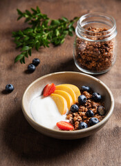 Fresh natural yogurt with homemade muesli; peach; strawberry and blueberry in a bowl on a dark wooden background close up. The concept of a healthy and nutritious breakfast. Healthy food