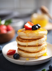 Homemade classic American pancakes in a stack with fresh berries and honey close-up on a blurry dark gray background. The concept of a healthy, delicious and nutritious breakfast