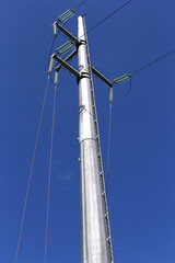 Close up of a modern eletric high voltage pole and power line against a very blue sky background in Italy. Vertical view