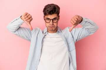 Young caucasian man isolated on pink background showing a dislike gesture, thumbs down....