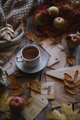 A cup of coffee stands on a wooden background, apples and autumn leaves are on the table.