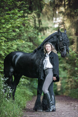 Happy young woman standing next to a frisian horse. - 460686545