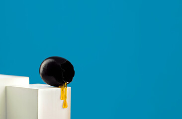 Cracked toxic black egg with dripping honey placed on white box.