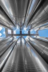 A row of stainless steel fermentation wine tanks against clouds and a blue sky. Steel wine tanks...