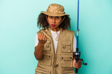 Young african american fisherwoman holding a rod isolated on blue background  showing fist to camera, aggressive facial expression.