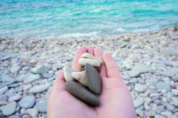 A girl holds pebbles on a stony beach by the sea. - obrazy, fototapety, plakaty