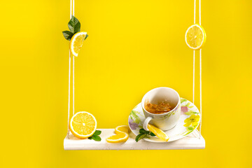 Tea mug sitting on a swing with lots of fresh cut lemon around and beautiful bright yellow background