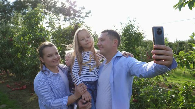 Happy family outdoors taking phone selfie picture on nature apple tree garden countryside parents with children daughters