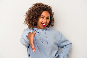 Young african american woman with curly hair isolated on white background stretching hand at camera in greeting gesture.