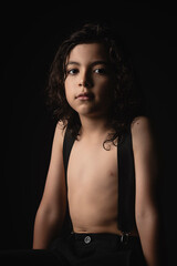 Hermoso niño sin camisa viendo a cámara en estudio con fondo negro
