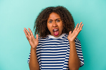 Young african american woman with curly hair isolated on blue background screaming to the sky, looking up, frustrated.