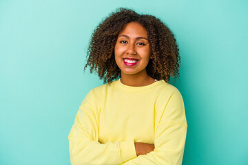 Fototapeta premium Young african american woman with curly hair isolated on blue background who feels confident, crossing arms with determination.