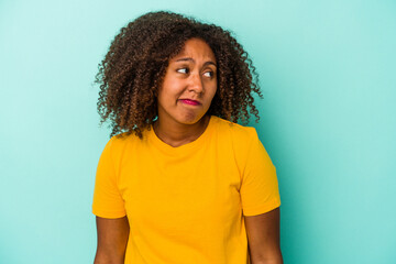 Fototapeta na wymiar Young african american woman with curly hair isolated on blue background shrugs shoulders and open eyes confused.