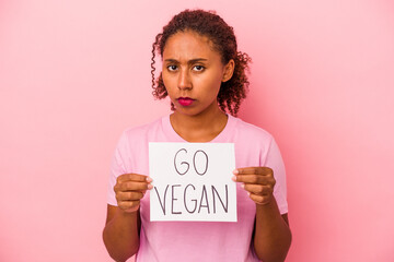 Young African American woman holding a go vegan placard isolated on pink background