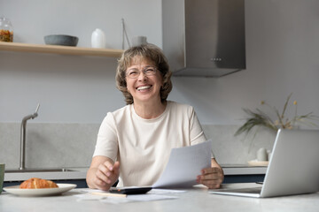 Portrait of happy senior old retired woman in glasses holding paper bills in hands, calculating household expenditures, planning household budget or investment, paying for medical insurance online.