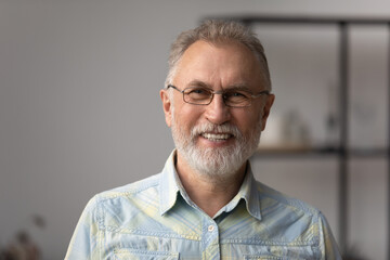 Head shot portrait of happy mature old retired man in eyewear posing indoors. Emotional smiling...