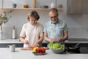 Happy bonding middle aged older retired family couple enjoying cooking meal together on weekend in kitchen, chopping fresh vegetables preparing vegetarian healthy food, involved in daily routine.