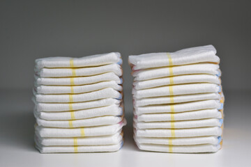 A stack of white disposable diapers with orange stripes. A stack of baby diapers on grey background. A large stack of baby diapers, close-ups, diaper packaging.