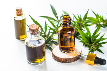 CBD oil in glass bottles and cannabis leaves at white table. Close up. Medicine and cosmetic product.