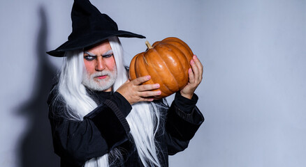 Handsome Man in witch costume with pumpkin in hand ready to Halloween party. Devil man. Magic hat.