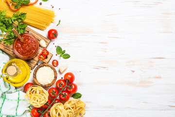 Italian food background. Pasta, tomato sauce, fresh tomatoes, parmesan, olive oil, herbs and spices at white kitchen table. Top view with copy space.