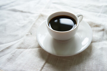 Morning coffee in a white cup on a white linen fabric