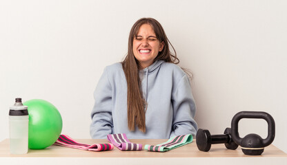 Young caucasian woman sitting at a table with sport equipment isolated on white background laughs and closes eyes, feels relaxed and happy.