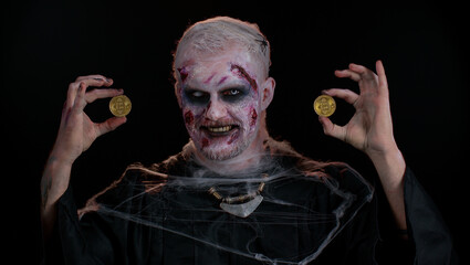 Zombie man with make-up with fake wounds scars showing golden bitcoins. Achievement career wealth, cryptocurrency investment, mining btc, future technology. Sinister dead guy. Halloween, filming