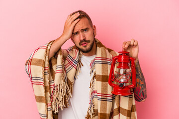 Young caucasian man with tattoos holding vintage lantern isolated on pink background  being shocked, she has remembered important meeting.