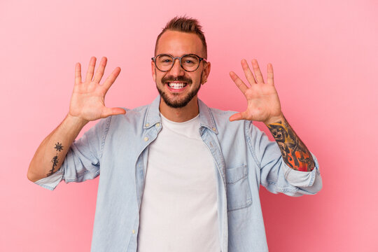 Young caucasian man with tattoos isolated on pink background  showing number ten with hands.