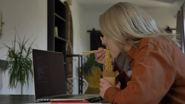 Smiling woman developer eating asian noodles in home office