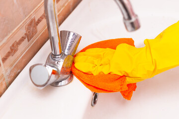 hand in a yellow rubber glove wipes the sink in the bathroom