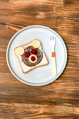 Funny bear face sandwich toast bread with peanut butter, cheese and raspberry on plate wooden background close up. Kids child sweet dessert breakfast lunch food