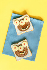 Funny monster face on halloween sandwich toast bread with peanut butter, cheese on napkin yellow background close up. Kids child sweet dessert breakfast lunch food