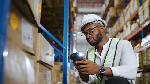 Warehouse worker working process checking the package with a barcode scanner in large warehouse distribution. African male supervisor inspects cargo delivery status.