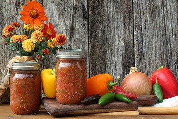homemade salsa in glass jars with fresh vegetables on a rustic wood background