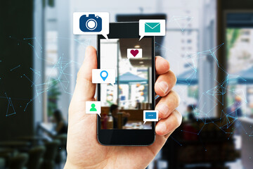 Close up of hand holding smart phone device with abstract polygonal mesh, camera, location pin, email and chat icons on blurry coworking interior background. 