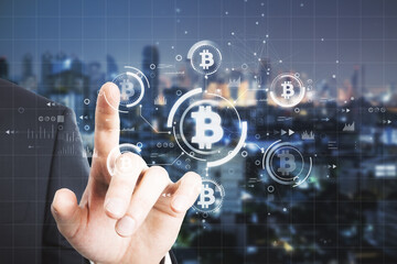 Close up of man hand pointing at abstract bitcoin hologram on dark night city background. Cryptocurrency, finance and blockchain concept. Double exposure.