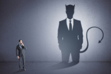 Fototapeta premium Attractive thoughtful young european male with devil shadow standing in empty concrete interior. Disguise, demon and career concept.