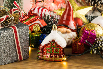 Wooden table with Christmas decorations. Red, silver and gold balls, gift boxes, lights, Santa Claus, Panettone, Christmas tree and others. Selective focus.