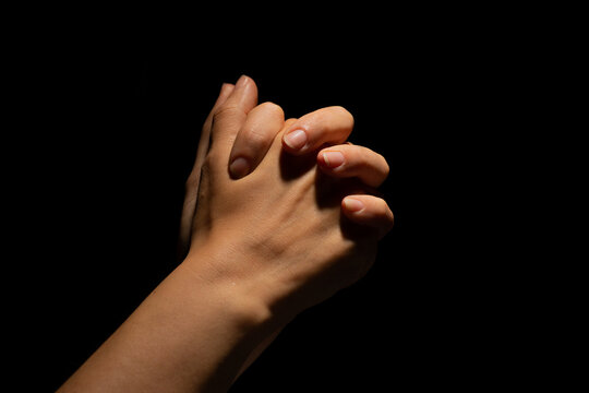 Praying crossed hands on a black background. Light from above. Hands folded in prayer. Hand gestures