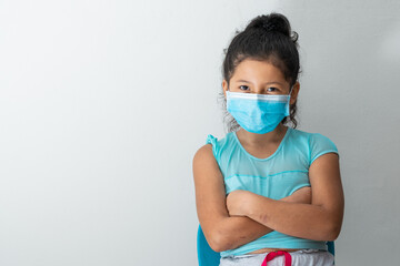 little girl (8 years old) looking at the camera with a malicious face, sitting with crossed arms and blue surgical mask. Medical, pharmaceutical and sanitary concept.