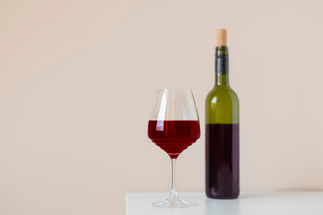 Red wine glass with dark wine bottle on white table. Simple interior with copy space